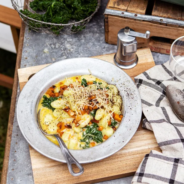 Creamy gnocchi with kale, walnuts, and cheese on a wooden table with a pepper mill and kitchen towel.