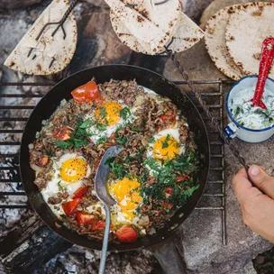 Lamb mince and eggs cooking in a frying pan on a campfire.