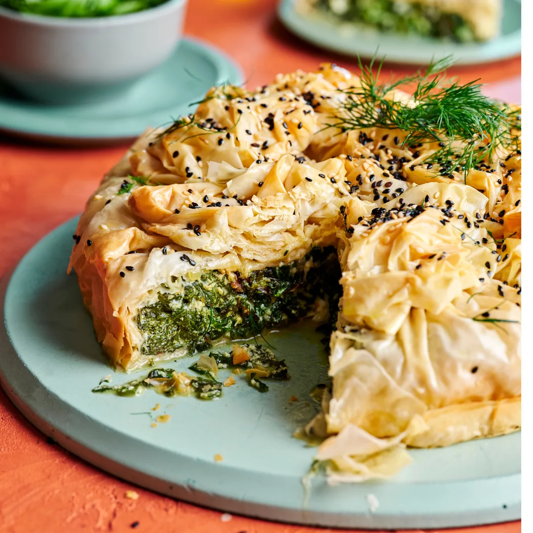 Greek greens pie with a slice cut out of the middle, showing the green filling like a spanakopita, or spinach pie.