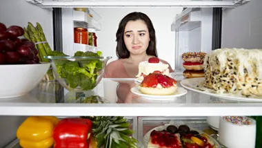 Women contemplates healthy versus unhealthy foods inside a fridge