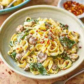 A bowl of creamy mushroom and spinach pasta topped with chilli flakes.