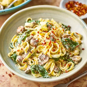 A bowl of creamy mushroom and spinach pasta topped with chilli flakes.