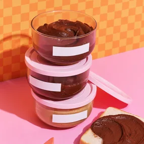 Three tubs piled together filled with chocolate spread, and a slice of bread smeared with chocolate spread.