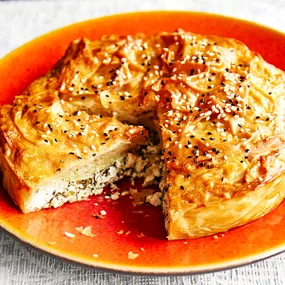 Herb and feta borek on a red plate with golden crispy pastry.