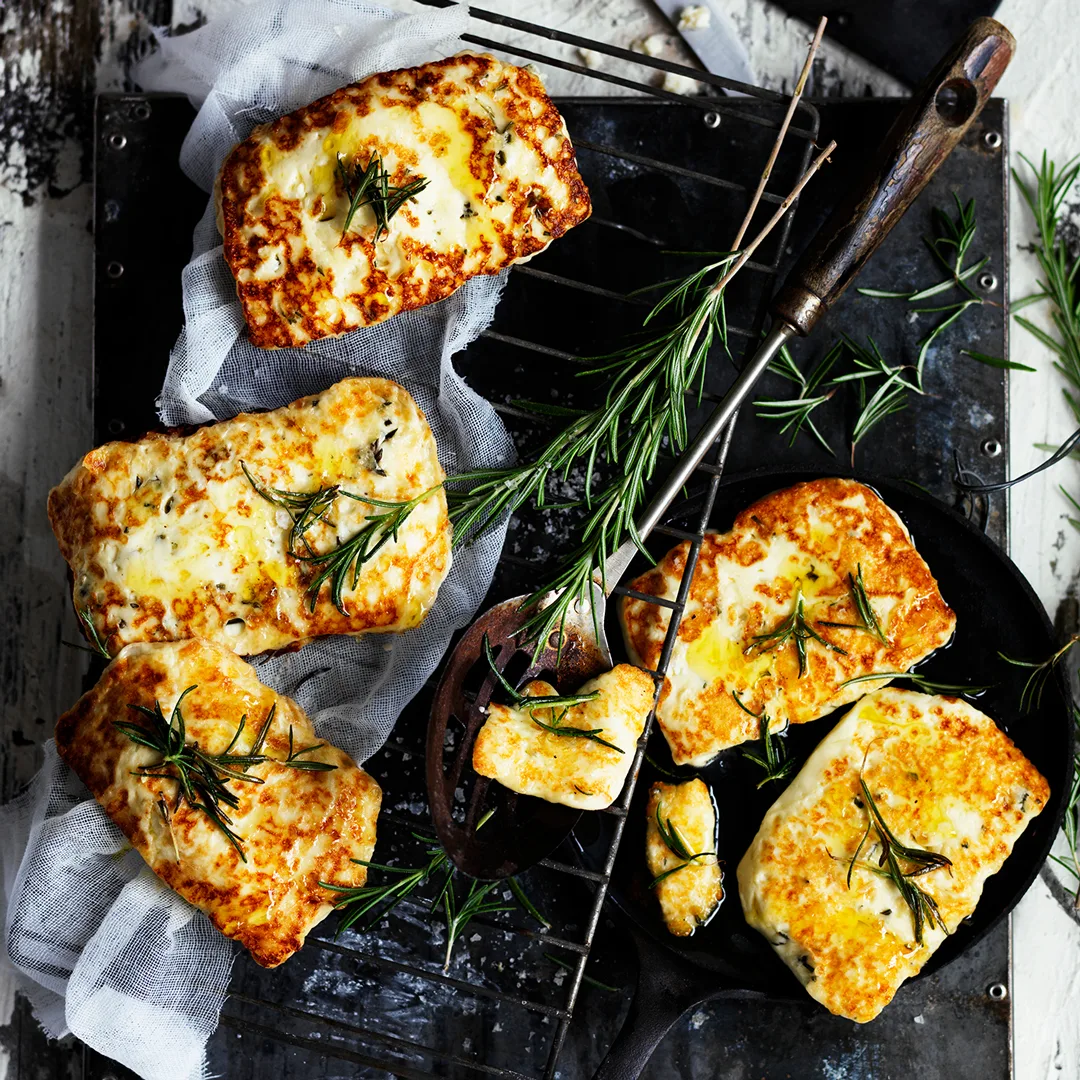 Five pieces of golden fried haloumi sprinkled with rosemary sprigs.