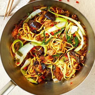 Pork and eggplant stir-fry in a wok with noodles and pak choi.