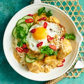 Potato rendang in a bowl, served with rice and a crispy fried egg. Garnished with cucumber and chilli.