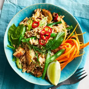 Thai fish cakes broken up in a bowl with fried rice, green beans, carrot, lime and chilli.