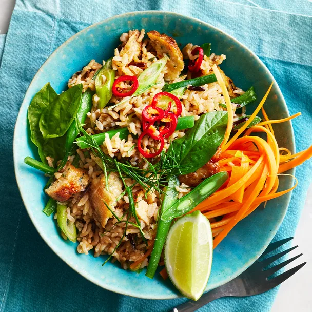 Thai fish cakes broken up in a bowl with fried rice, green beans, carrot, lime and chilli.