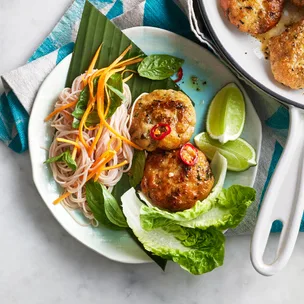Two Thai fish cakes in a bowl with vermicelli salad, carrots and lettuce.