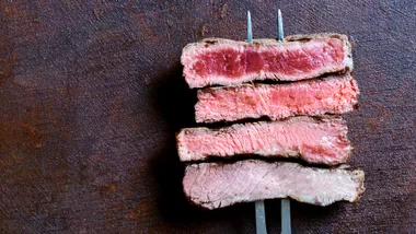 Four pieces of red meat, such as a cut of a steak, cooked and skewered on a fork.