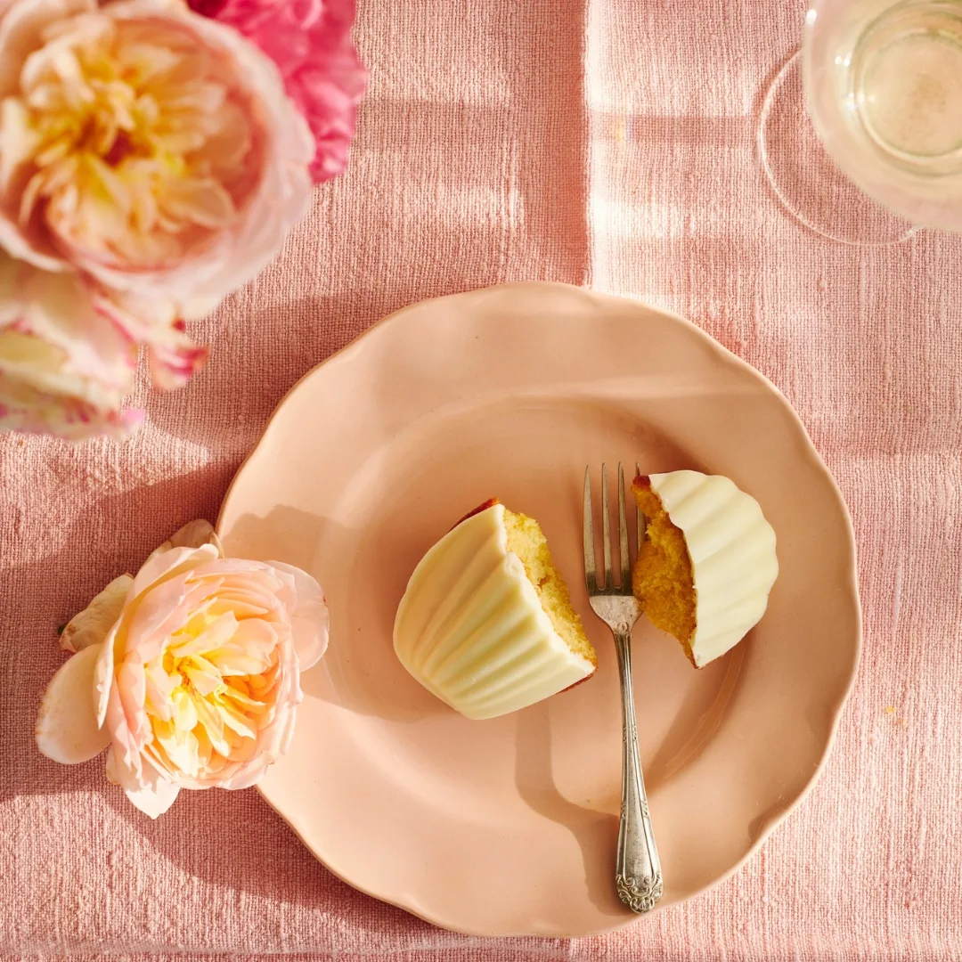 madeleines split in half with a white chocolate topping on a pale pink plate with a fork