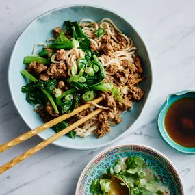 Dan dan noodles in a blue bowl with gai lan and green onion sauce.