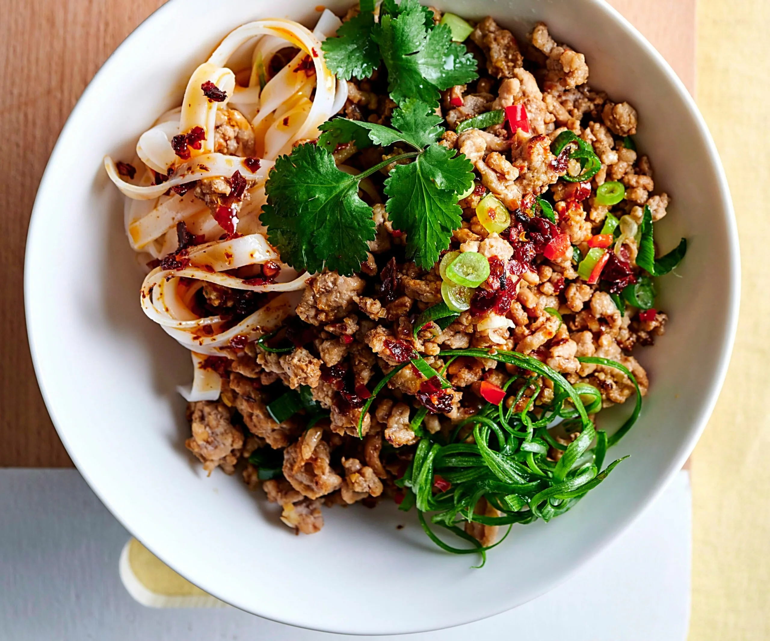 Bowl of noodles with minced meat, chili oil, cilantro, and sliced green onions.