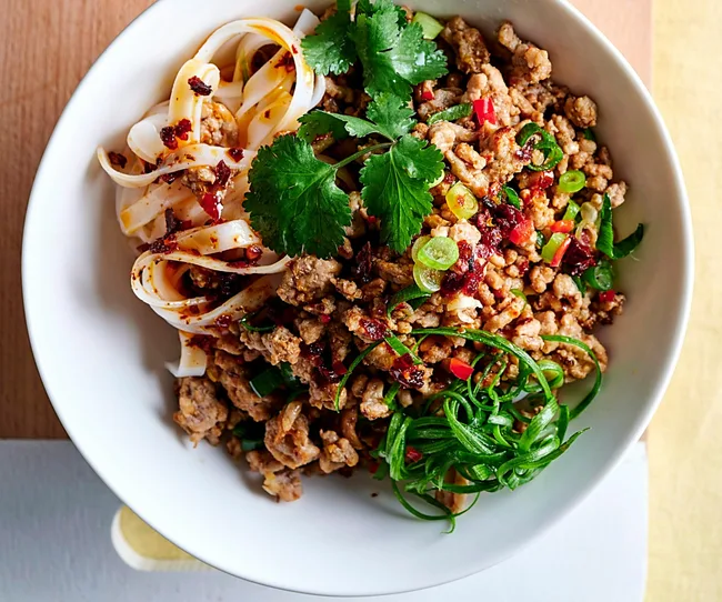 Bowl of noodles with minced meat, chili oil, cilantro, and sliced green onions.