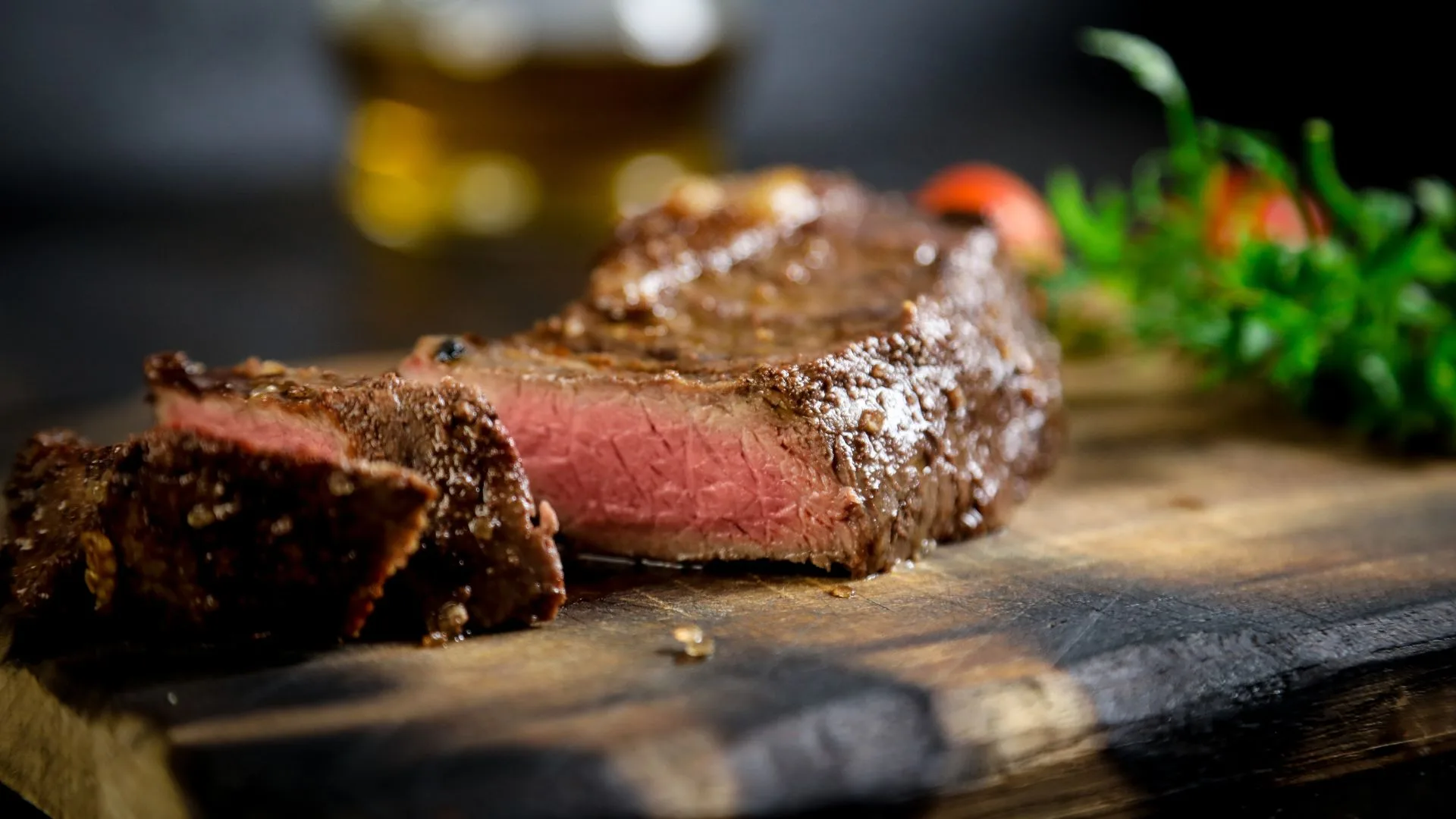 Sliced medium-rare steak on a wooden board with blurred greenery in the background.