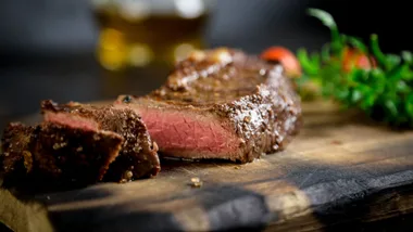 Sliced medium-rare steak on a wooden board with blurred greenery in the background.