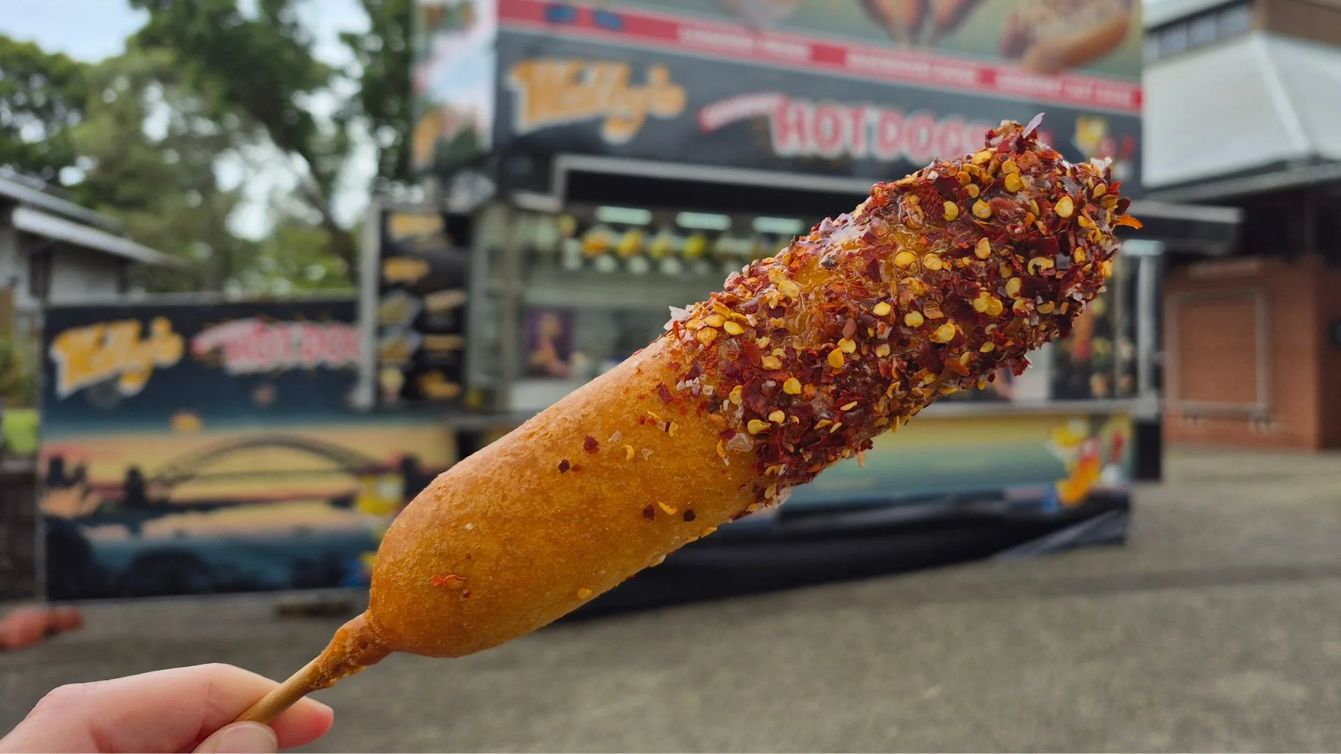 hot honey corn dog covered in chilli flakes on a stick in front of a food truck in the Royal Easter Show 2026 showground