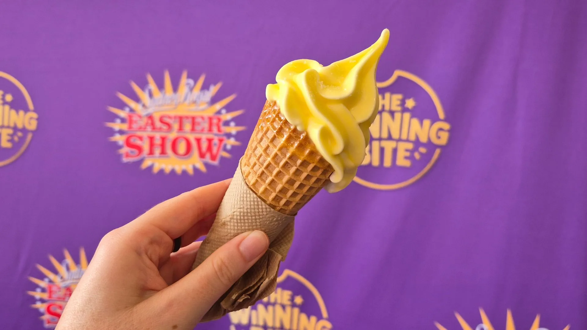 Butter-dipped Soft Serve in a cone held in front of a Royal Easter Show 2026 banner