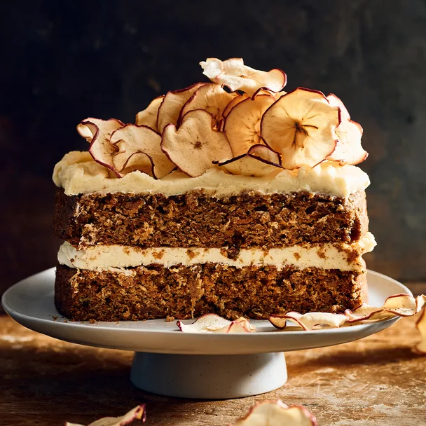 A slice of apple and carrot cake with brown butter icing and dried apple slices on top