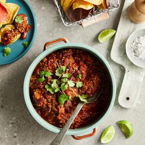 Slow cooker chilli con carne served with with corn chips and lime wedges