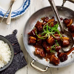Caramelised pork belly bites on a serving dish with a side bowl of steamed white rice