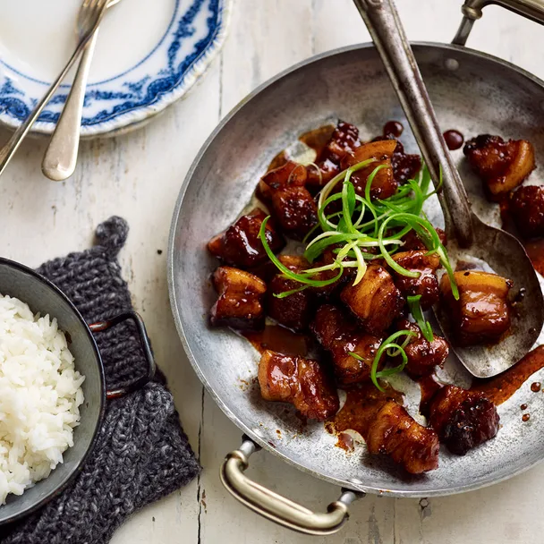Caramelised pork belly bites on a serving dish with a side bowl of steamed white rice