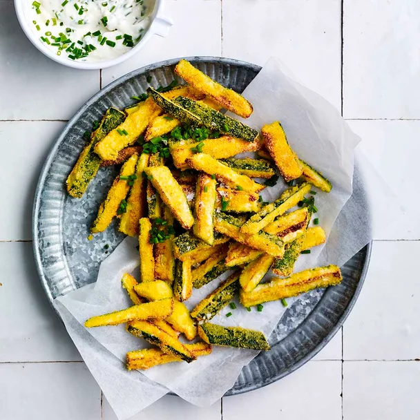 zucchini fries on a plate with a bowl of yoghurt sauce alongside