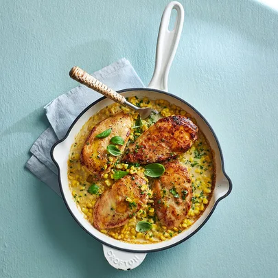 chicken dinner recipe of four chicken breasts on a creamy corn sauce in a pan