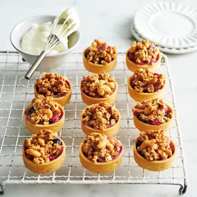 small tartlets filled with apple and berries and topped with crumble, on a baking tray