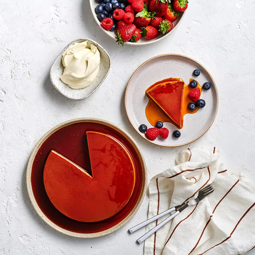 Whole creme caramel and a slice on plates with berries