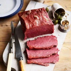 Corned beef cooked in the pressure cooker, on a chopping board, sliced, with caper berries