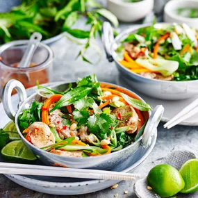 Two bowls of pork stir fry with lime and peanuts with sweet chilli dressing and cut limes on the side