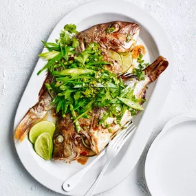 Air fryer whole snapper topped with green onion, coriander, snow peas and ginger on a platter