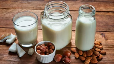 Alternative types of vegan milks in glass bottles on rustic wooden table.