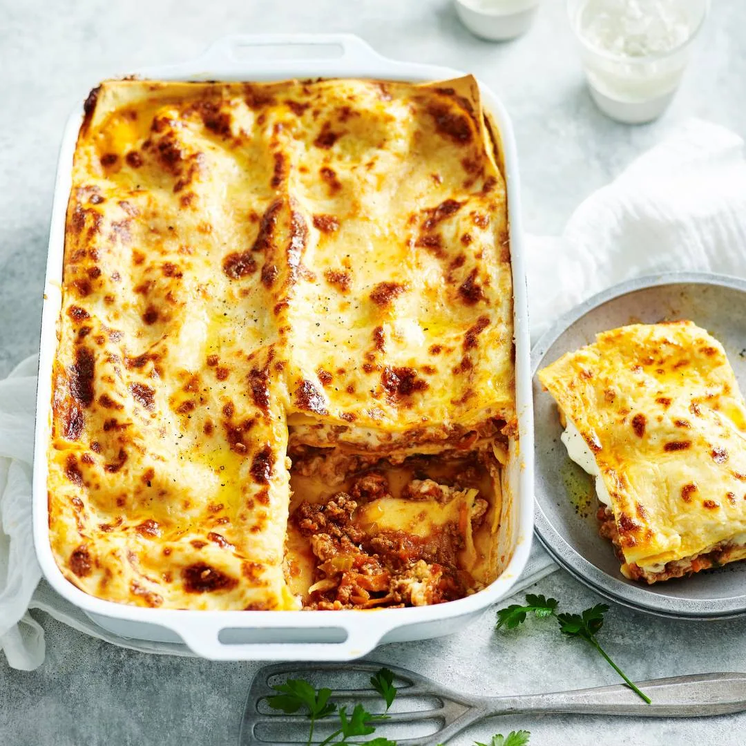 classic beef lasagne in a baking tray with a slice on a plate