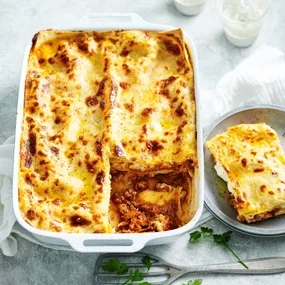 classic beef lasagne in a baking tray with a slice on a plate