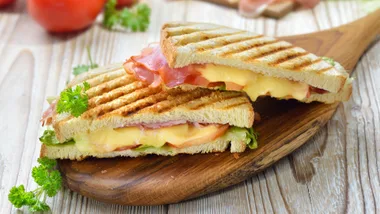 Grilled and pressed toast with smoked ham, cheese, tomato and lettuce served on sandwich paper on a wooden table