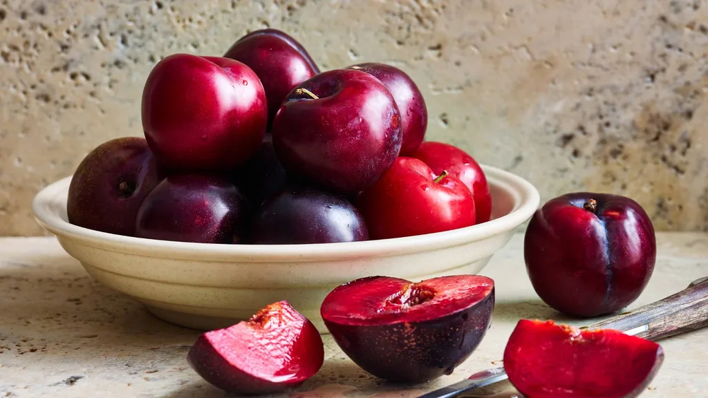 Plums in a bowl and sliced plums on bench
