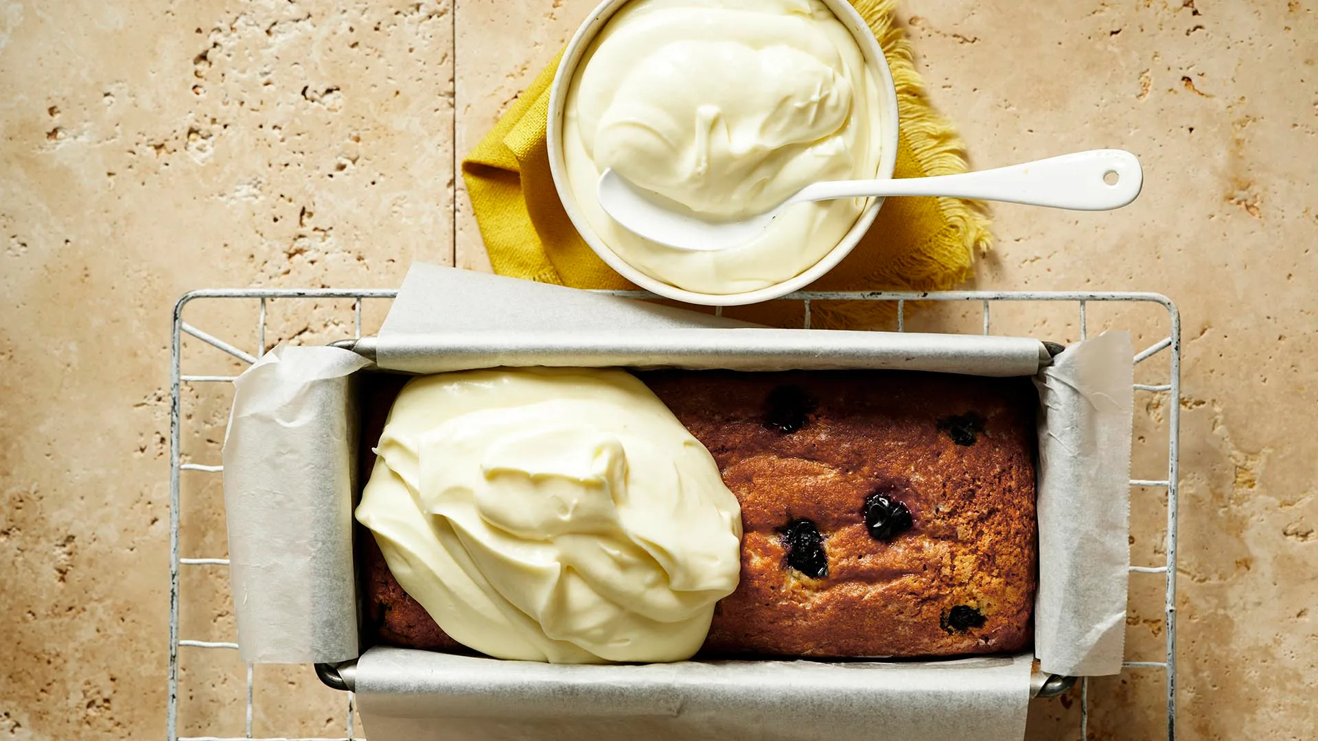 lemon blueberry cake being iced in the tin with mascarpone icing