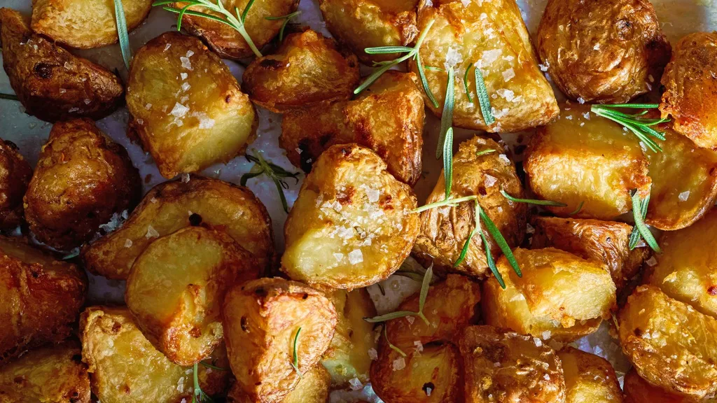 A close up image of the best roast potatoes with rosemary sprigs