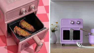 A split image showing the Crumble air fryer. On the left, a pink air fryer has its basket pulled out, revealing two pieces of cooked steak on a grill insert. On the right, a purple version of the air fryer is shown on a kitchen counter next to a vase of daisies and a pot.