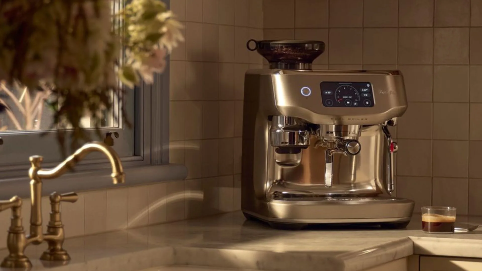 A shiny gold espresso machine (Breville Barista Oracle Dual Boiler) on a kitchen counter next to a sink.