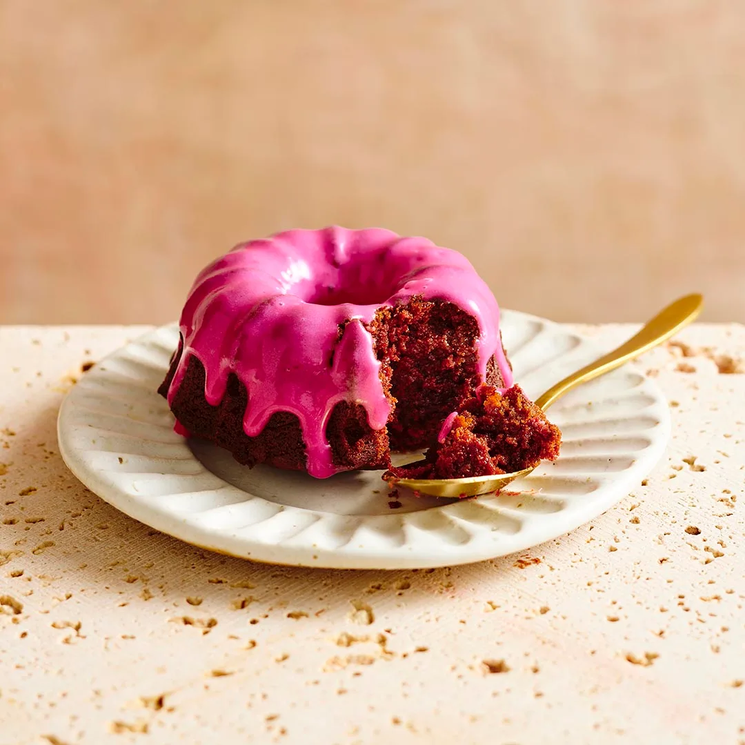 A single beetroot chocolate mini bundt cake with vivid pink icing, with a spoonful taken out