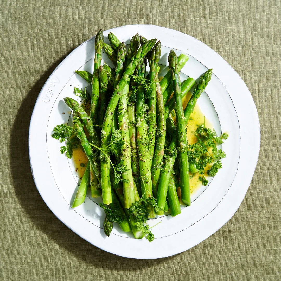 Asparagus with chervil vinaigrette on a white plate over a green cloth.