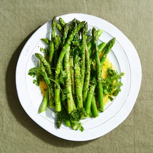 Asparagus with chervil vinaigrette on a white plate over a green cloth.