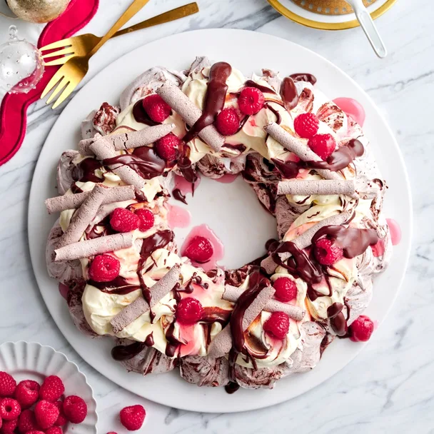 Christmas chocolate meringue wreath topped with raspberries, cream and chocolate sauce.