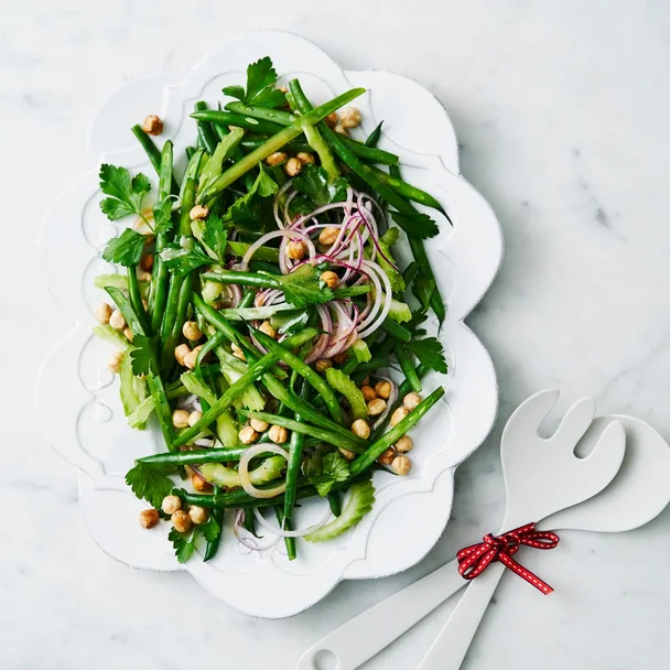 Green bean salad recipe with French dressing on a white serving platter, with salad servers.