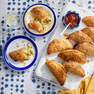 Ham, broccoli, mustard & cheddar hand pies on a platter, with a bowl of tomato sauce.