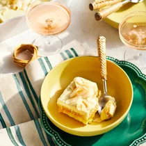 A slice of limoncello tiramisu with passionfruit curd in a yellow bowl with a spoon.